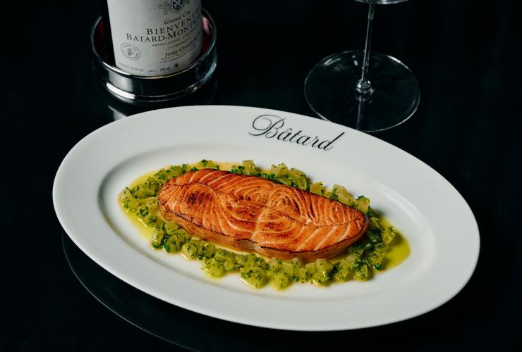 带 Bâtard 标记的盘子里盛着油封三文鱼配蔬菜丁,旁边放着一瓶葡萄酒。© Maison Bâtard 版权所有