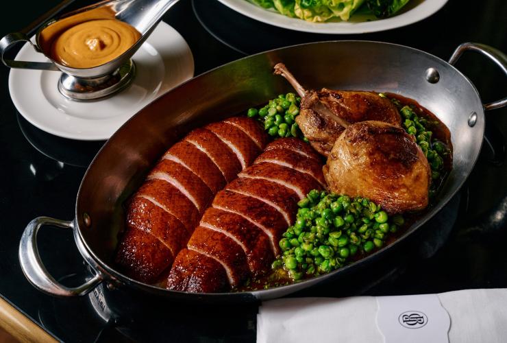 黑色餐桌上摆放着一盘烤鸭胸与鸭腿配豌豆,以及一个酱汁碟。© Pete Dillon 版权所有