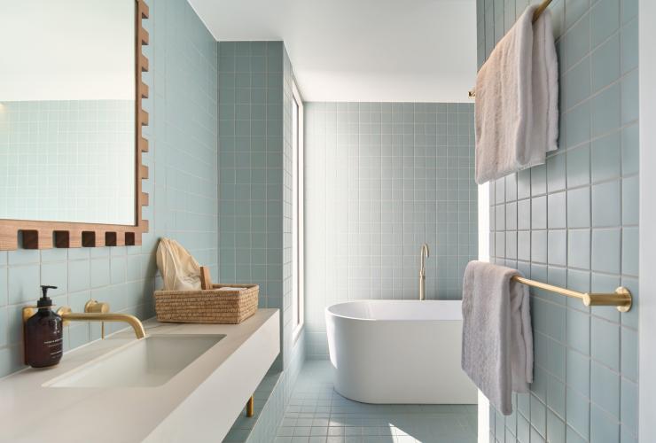 卫生间内景,墙面铺设蓝色方块瓷砖,左侧是洗手台和镜子,另有一个独立浴缸。© Shot By Thom 版权所有