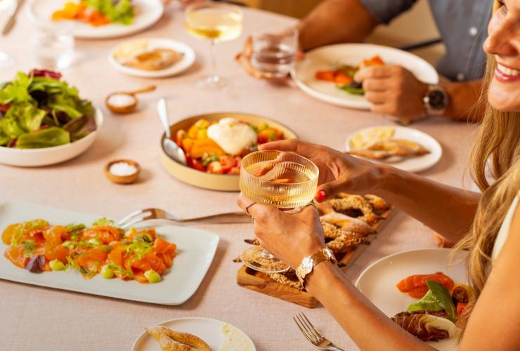 摆放着美食的餐桌,一位女性手握玻璃杯。© Saltbox 版权所有